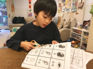 Child cutting out game cards on Chinese worksheet