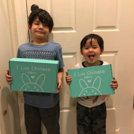 Two multiethnic Asian American boys holding I Luv Chinese boxes while standing against a door.